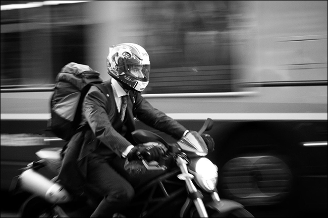 Mann im Anzug, der Motorrad mit verschwommenem Bus fährt, der sich hinter ihm bewegt