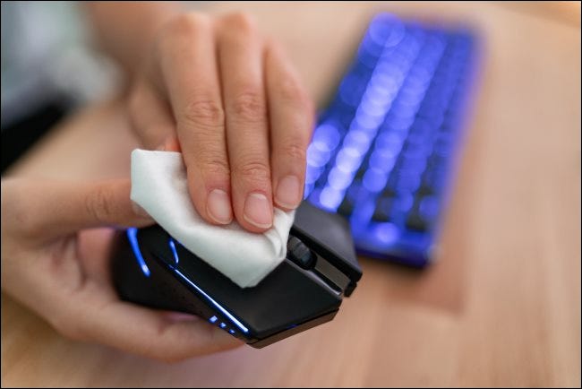 Eine Hand, die eine Computermaus mit einem Tuch abwischt.